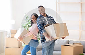 Young black homeowners with carton boxes feeling happy in their new home on moving day, panorama