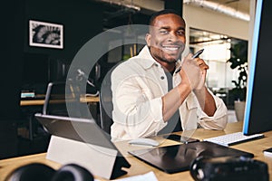 Young Black Male Advertising Marketing Or Design Creative In Modern Office Sitting At Desk Working On Computer Smiling to Camera