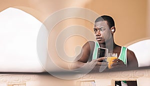 Young black male enjoying an ice-cold drink while listening to music on his smartphone