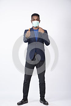 Young black male wearing a suit and face mask giving a thumbs-up and pointing to the mask