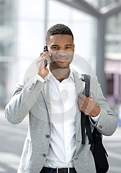 Young black man with bag talking on mobile phone