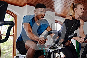 Young black man and caucasian woman doing cardio workout on exercise bike at the gym