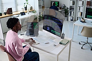 Young Black Man Coding on Computer in Office with Multiple Monitors