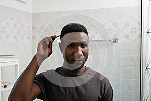 Young Black Man Combing Hair Looking at Camera