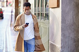 Young black man consulting his phone while walking down the street.