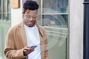 Young black man consulting his phone while walking down the street.