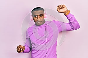 Young black man dancing listening to music using headphones relaxed with serious expression on face