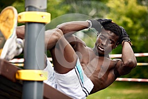 Young black man doing crunches outdoors. He is in a park.