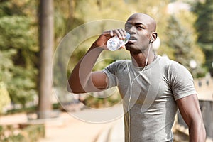 Young black man drinking water before running in urban background