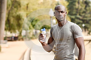 Young black man drinking water before running in urban background