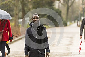 Young Black Man with Earphones on Park Road with Incidental People