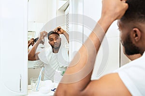 Young black man examining his hair, looking at bathroom mirror