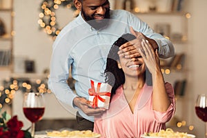 Young black man giving box to woman, covering eyes