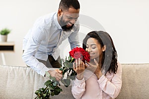 Young black man giving bunch of red roses to woman