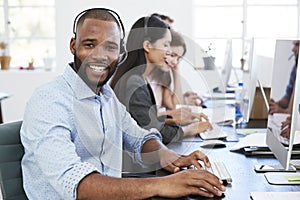 Young black man with headset on smiling to camera in office
