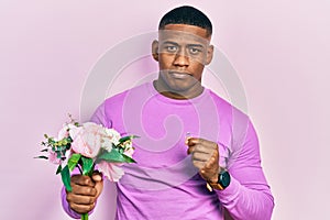 Young black man holding bouquet of flowers and wedding ring relaxed with serious expression on face