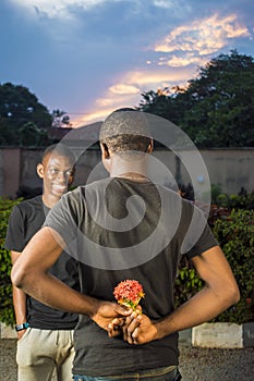 young black man holding flowers behind his back waiting to surprise his lover