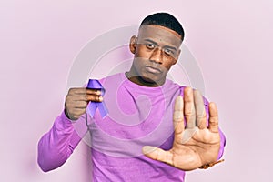Young black man holding purple ribbon awareness with open hand doing stop sign with serious and confident expression, defense