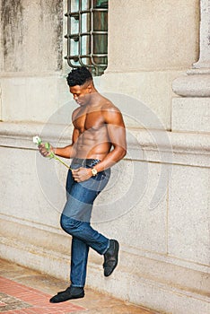 Young black man holding white rose, standing outdoors in New York City, looking down, thinking