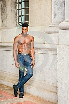 Young black man holding white rose, standing outdoors in New York City, looking forward
