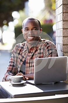 Young black man with laptop outside a cafe looking to camera