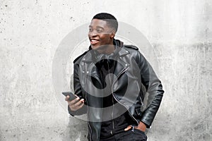 Young black man in leather jacket smiling while holding cellphone
