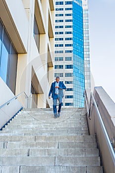 Young black man looking at wristwatch, walking down stairs outside office building in New York City