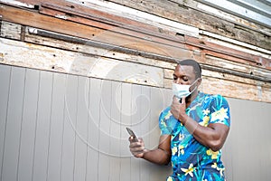 A young black man with a mask in the covid-19 pandemic season for protection. African American man with cell phone.