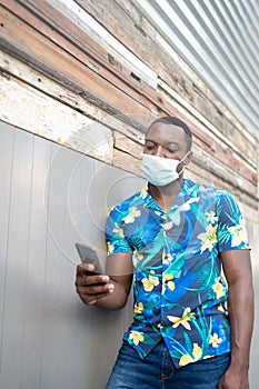 A young black man with a mask in the covid-19 pandemic season for protection. African American man with cell phone.