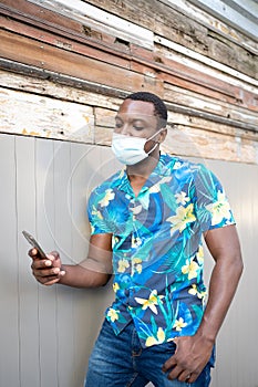 A young black man with a mask in the covid-19 pandemic season for protection. African American man with cell phone outdoors.