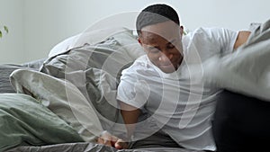 Young black man person waking up at bedroom. Happy african guy stretching in bed in morning. Young adult smiling after