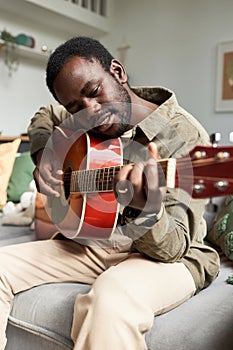 Young Black man playing guitar and enjoying free time in cozy home