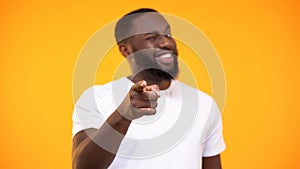 Young black man pointing finger on camera and smiling against yellow background