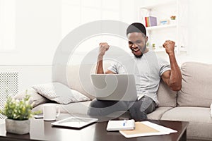 Young black man with raised arms, with laptop celebrating success