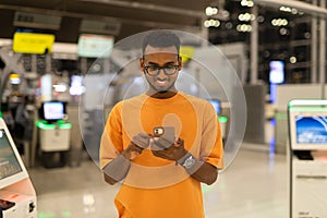 Young black man ready to travel at airport terminal waiting for flight while using phone