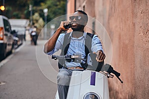Young black man on scooter with mobile phone