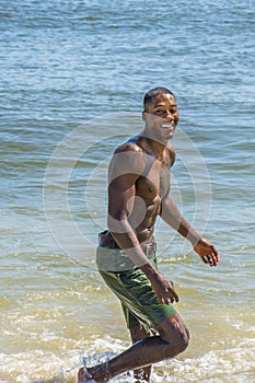 Young black man, shirtless, walking on beach, smiling, looking around