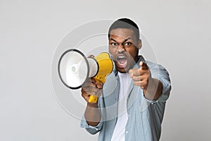 Young black man shouting in megaphone over grey background