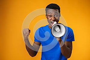 Young black man shouting in megaphone on yellow background