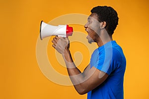 Young black man shouting in megaphone on yellow background