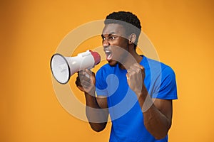 Young black man shouting in megaphone on yellow background