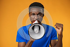 Young black man shouting in megaphone on yellow background