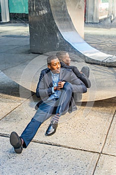 Young black man sitting  on ground against mirror outdoors in New York City, relaxing