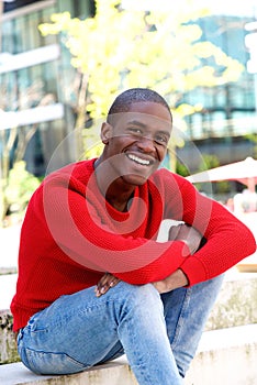 Young black man sitting outside smiling.