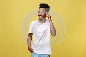 Young black man smiling and talking on mobile phone with copy space over yellow background.