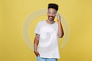 Young black man smiling and talking on mobile phone with copy space over yellow background.