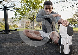 Young black man in sports clothing sitting and exhaling while doing stretches in park photo