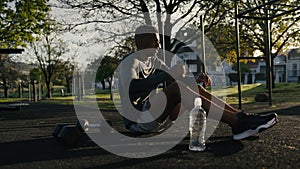Young black man in sports clothing taking a break after exercise with dumbbell in park