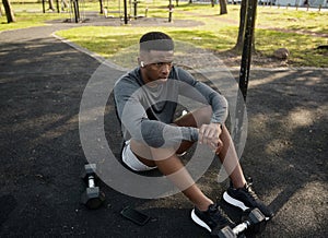 Young black man in sports clothing with wireless earphones sitting taking a break in park