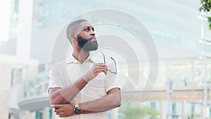 Young black man stand in the street and takes off his glasses thinking about his next business idea in architecture